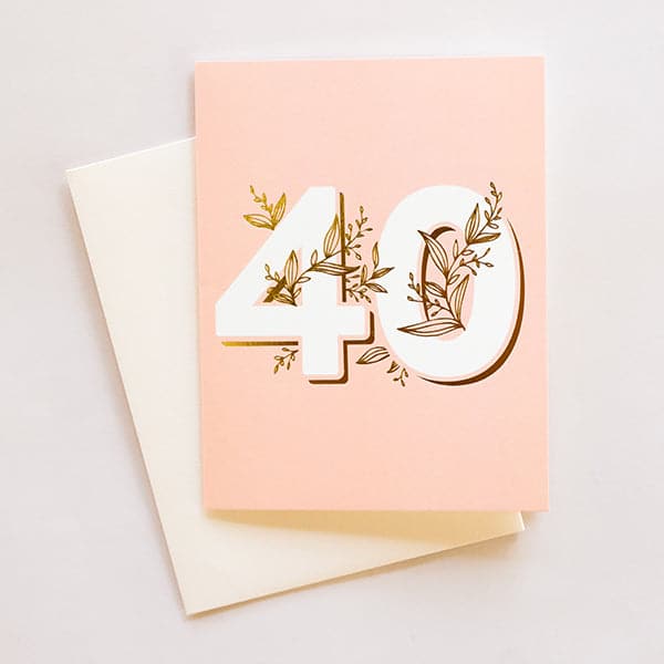 A light blush pink card with the numbers "40" in the center with gold foiled vining wrapped around and throughout it along with a white envelope.