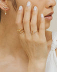 A gold ring with an open front that features a cubic zirconia on one end and a crescent moon on the other, photographed worn on a models hand.