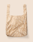 Photographed in front of a white background is a light tan / pink nylon reusable bag with a cream outlined Banana Leaves print on the front and back.