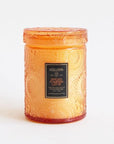 In front of a white background is an orange glass, cylinder jar. The glass has a floral texture. On the front is a black sticker with gold text that reads ‘voluspa.’ Below is orange text that reads ‘spiced pumpkin latte.’ On top of the jar is a matching glass lid.