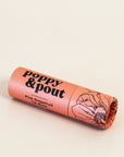 In front of white background is a round peach tube. On the right side is a black drawing of a flower. On the right side is black text that reads ‘poppy & pout, pink grapefruit lip balm.'
