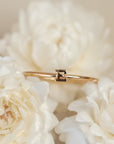 On a cream background is a dainty gold ring with an "E" in the center.