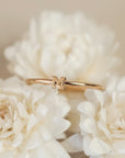 On a cream background is a dainty gold ring with an "M" in the center.