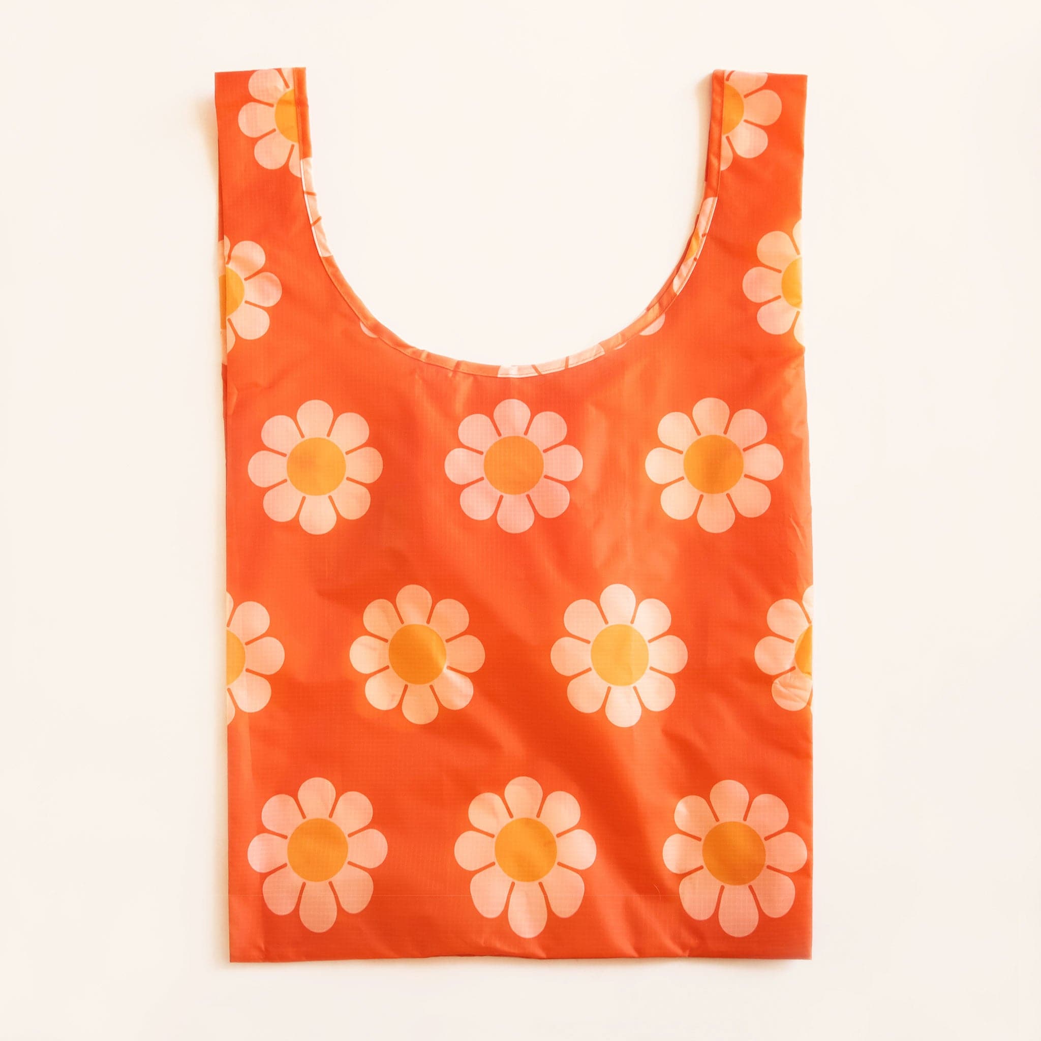 Red-orange reusable covered in a print of simple flowers with white petals and orange centers. The bag is positioned flat on a table and has a &#39;U&#39; shape between two handles.