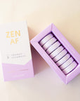 Eight lilac purple shower steamer tablets inside of a purple and white box that reads, "Zen AF" in gold text across the front.