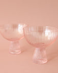 A light pink beveled coupe glass with a ribbed stem and a wider ribbed cup.