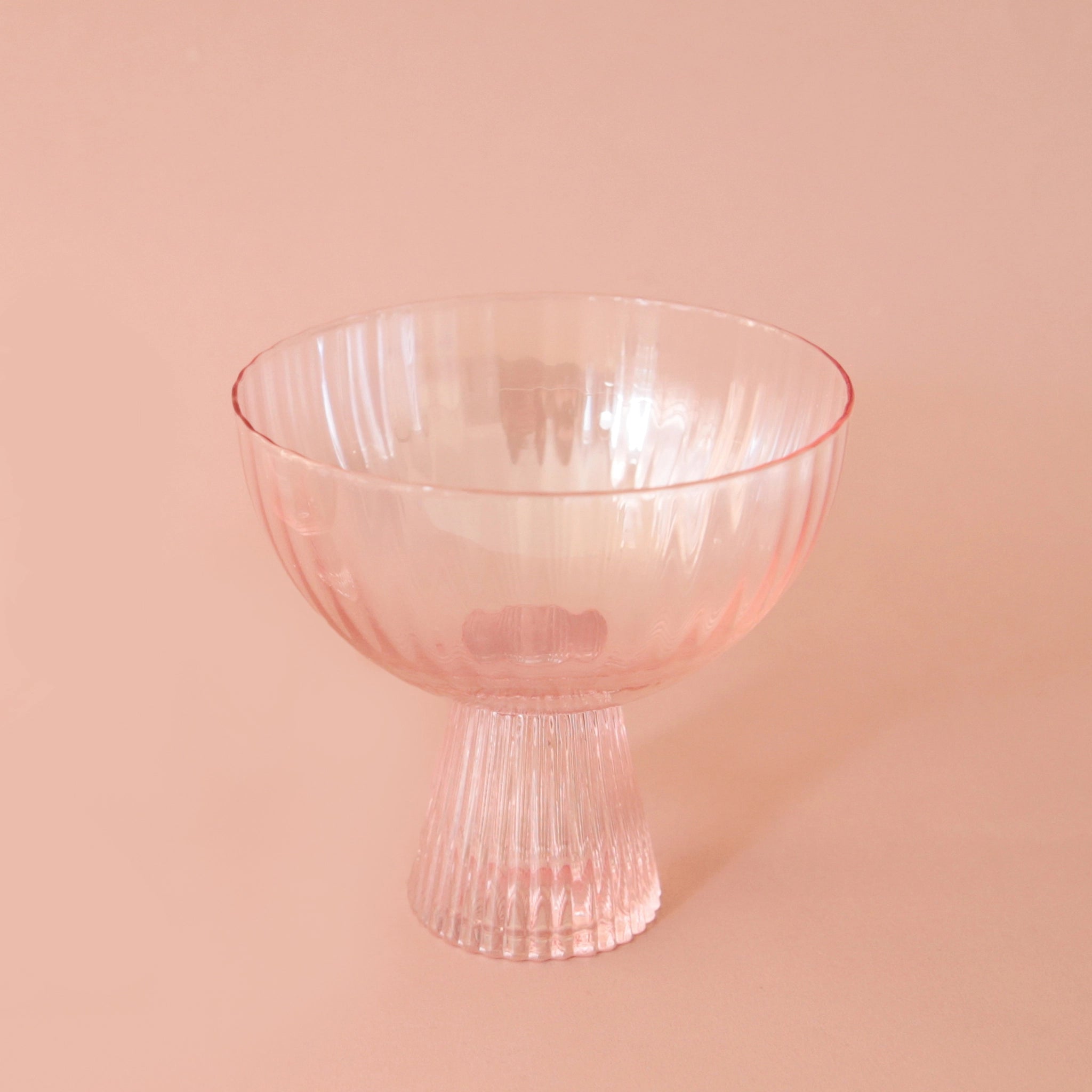 A light pink beveled coupe glass with a ribbed stem and a wider ribbed cup. 