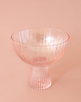 A light pink beveled coupe glass with a ribbed stem and a wider ribbed cup.