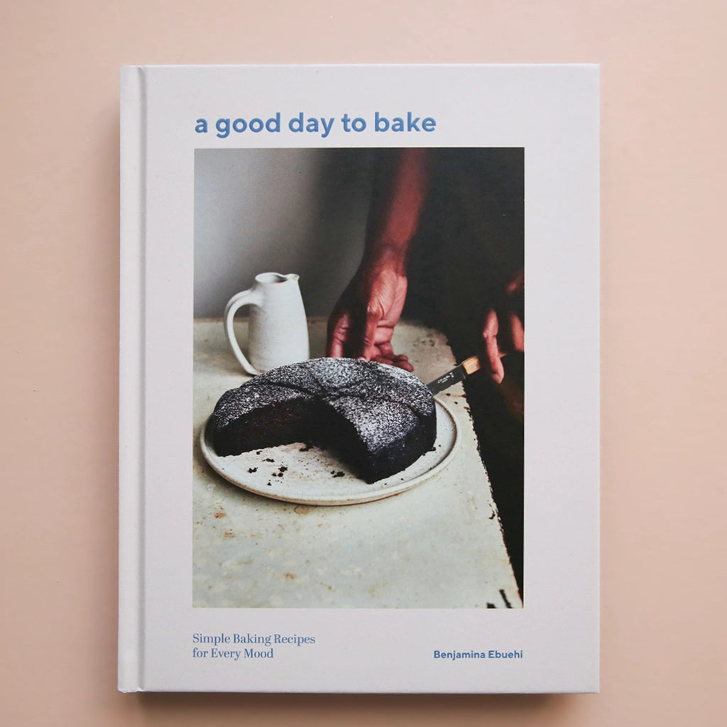 A white book cover with a photograph of a chocolate cake being cut along with the title that says, "a good day to bake" in light blue font.