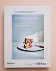 A white book cover with a photograph of a chocolate cake being cut along with the title that says, "a good day to bake" in light blue font.