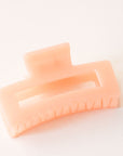 On a white background is a light orange colored rectangular claw clip with a jelly, almost translucent effect.