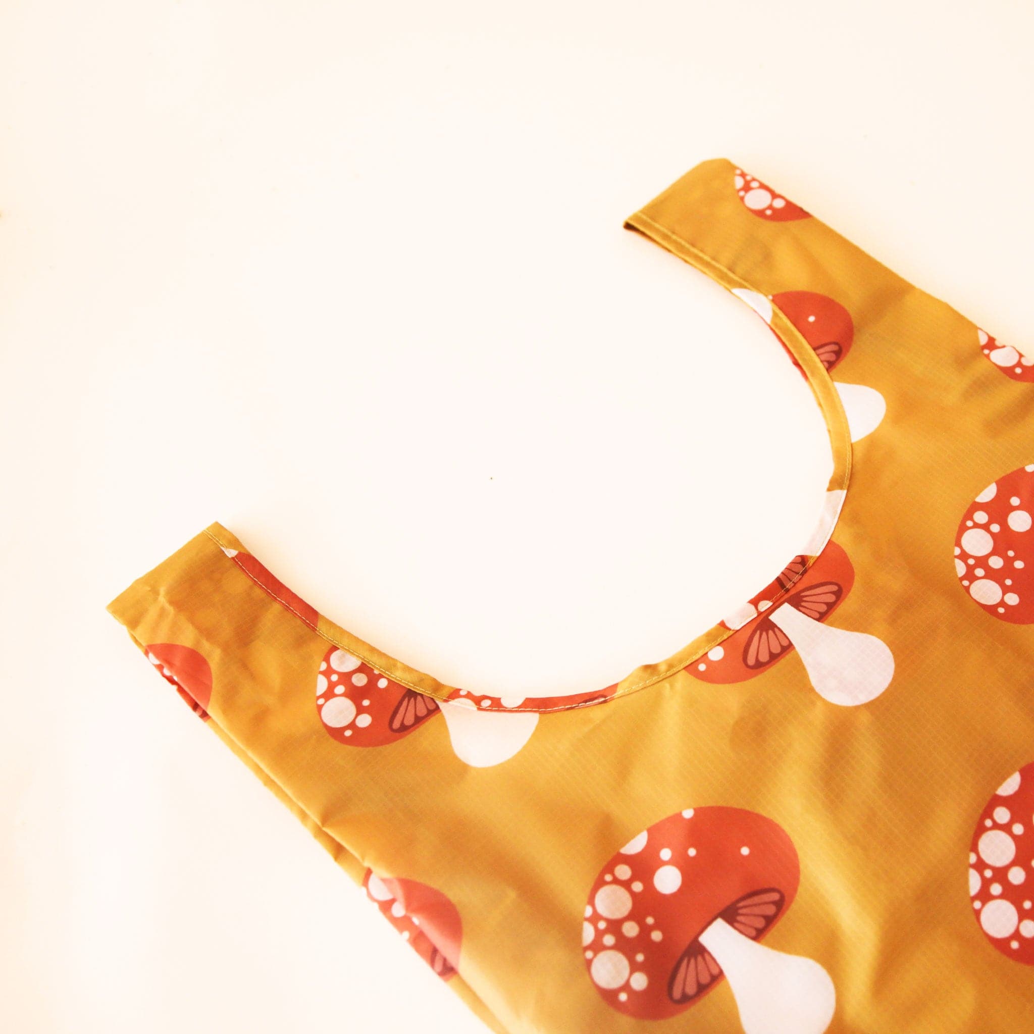 A mustard yellow nylon bag with reddish and cream mushroom print. 