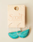 In front of a cream background is a pair of silver hoops. The bottom half of the hoop is a turquoise stone. The hoops are on a peach leather tag. Etched into the tag is text that reads ‘Scout curated wears.'
