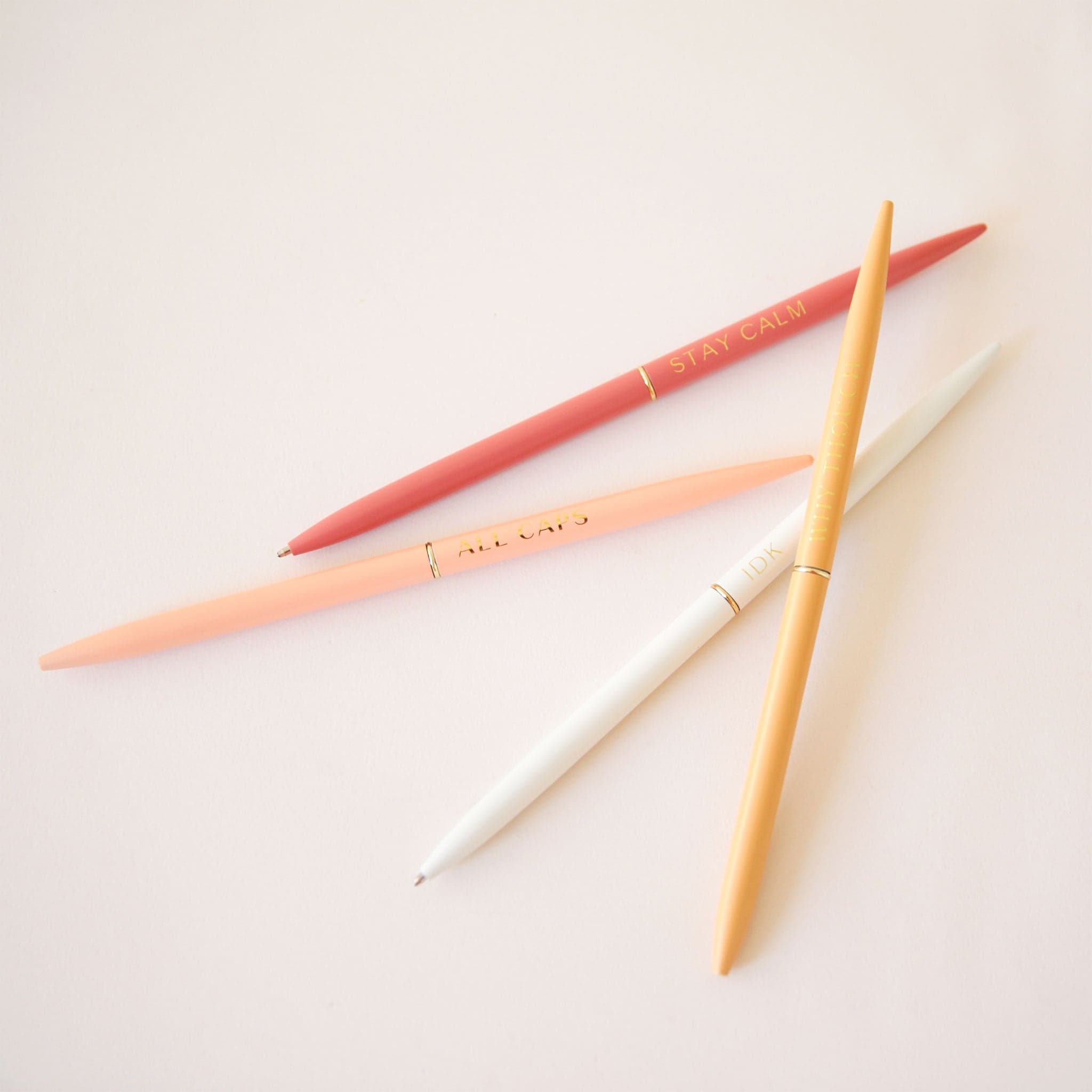 A set of 4 slender pens in yellow, white, salmon and rust. Each pen says something different. The rust pen says, &quot;Stay Calm&quot;. The salmon pen says, &quot;All Caps&quot;. The white pens says, &quot;Idk&quot;. And the yellow pen says, &quot;Why Though&quot;.