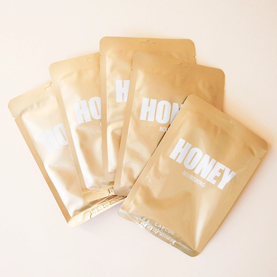5 gold pouches that contain a face mask. pouch reads &quot;honey nourishing&quot;.