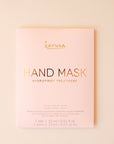 On a cream background is a pink packet with a hand mask inside that reads, "Karuna Hand Mask Hydrating + Treatment".