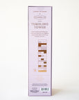 Against a white background is a light purple box with a set of wood blocks stacked upon one another ranging from white to shades of pink, red, and yellow along with letters at the top of the box that read, "Tumbling Tower". The back of the box showing the contents of the box which include 1 game die, 57 wooden blocks and instructions.