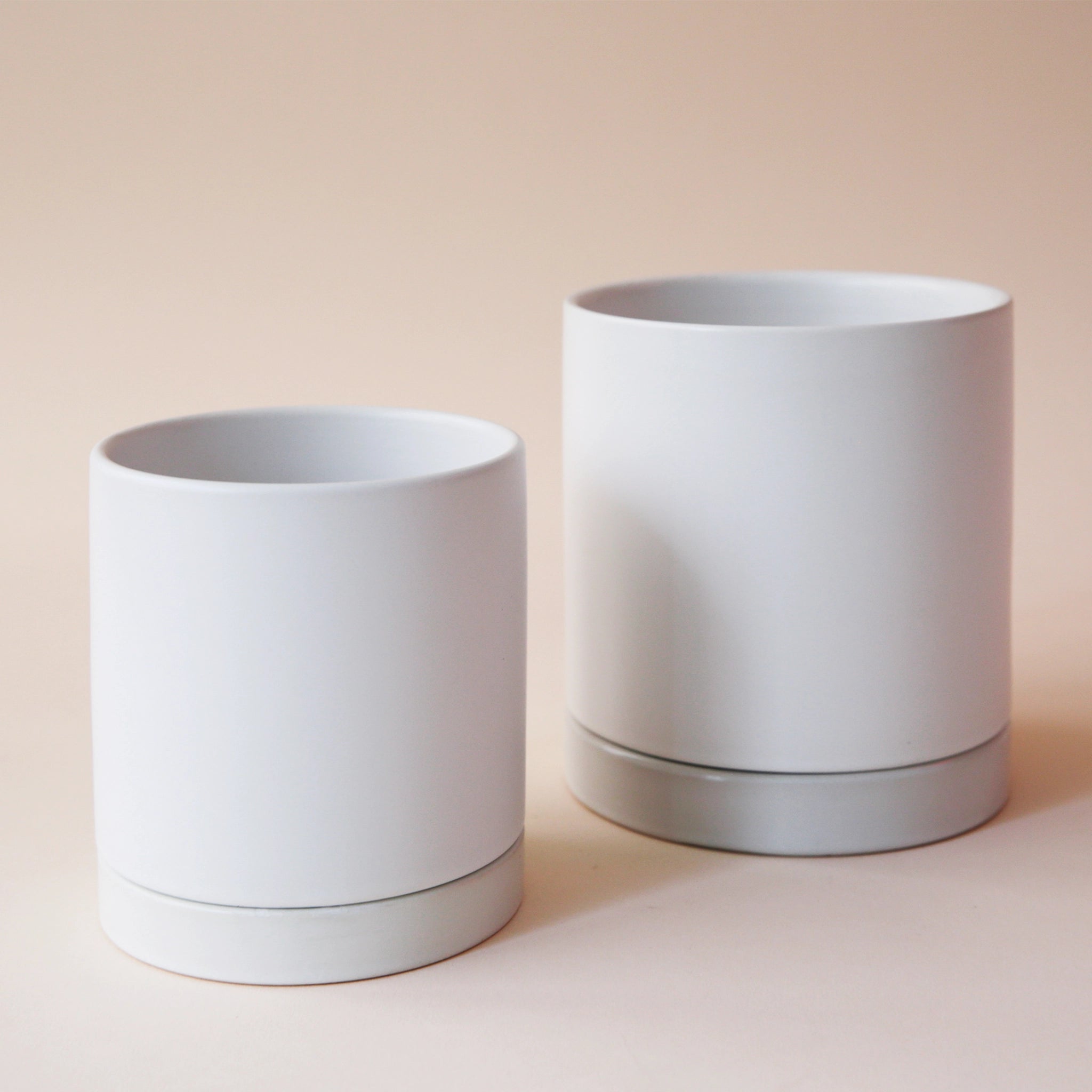 two simple white pots with matching saucers sit side by side on a pink ground