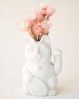 A ceramic lucky cat vase in white with its paw up in the waving position staged here with natural dried florals.
