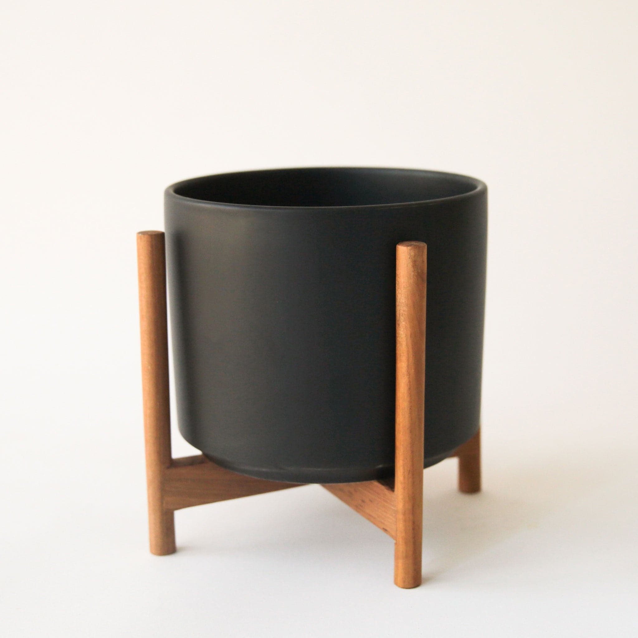 A black ceramic pot on a wooden stand with four legs.
