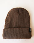 On a cream background is a brown ribbed beanie with a small black Brixton label on the edge of the folded brim.
