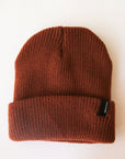 On a cream background is a rust colored ribbed beanie with a small black Brixton label on the edge of the folded brim.