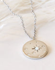Round star opal necklace in Silver. This necklace has a delicate gold chain, with a coin pendant. The pendant has a twinkle star impression with a set opal in the center. This star shape is off-center with other star impressions in a natural display with different sizes scattered across the pendant.