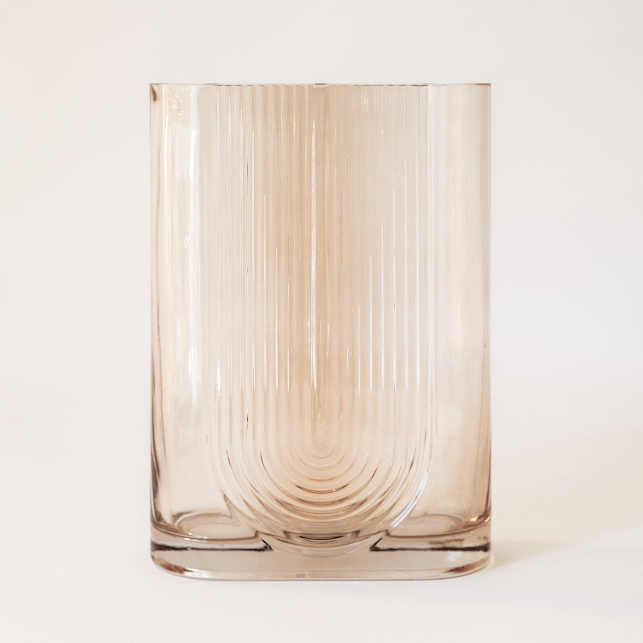 The morena vase in large alone. The morena vase has a unique shape. It is made from glass and has an oblong opening. The body of the vase is tall and angular resembling a square or rectangle, but with a pill-shaped opening the same width as the vase. There is a design on the front resembling a boho, upside-down rainbow design.