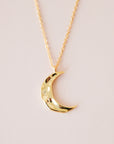 A gold dainty necklace with a crescent moon pendant with a wavy texture.