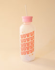 A glass water bottle with the word "HOWDY" in pink western style letters ,stacked five times at an angle on the front, a pink silicone lid with a straw coming out of the top.