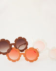 Brown flower shaped sunglasses with light brown circle lenses in the center photographed here with the other color ways available. One is an orange frame with a light orange lens and the other a white frame with a light pink lens.