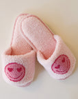 Pink fuzzy slide slippers with a darker pink heart eyes smiley face graphic on the front of each slipper.
