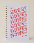 A light purple / cool toned pink notebook with the word "Howdy" slightly angled and stacked six times in pink western font and featuring a spiral bound detail.