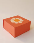 In front of a cream background is orange gift boxes with one VW bus daisy graphic.
