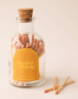 A glass jar of matches with a gold arched label and a cork cap.