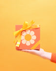 In front of a yellow background is orange gift boxes with one VW bus daisy graphic.