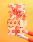In front of a yellow background is a stack of three orange gift boxes with red and yellow daisies and a red bow not included with purchase.