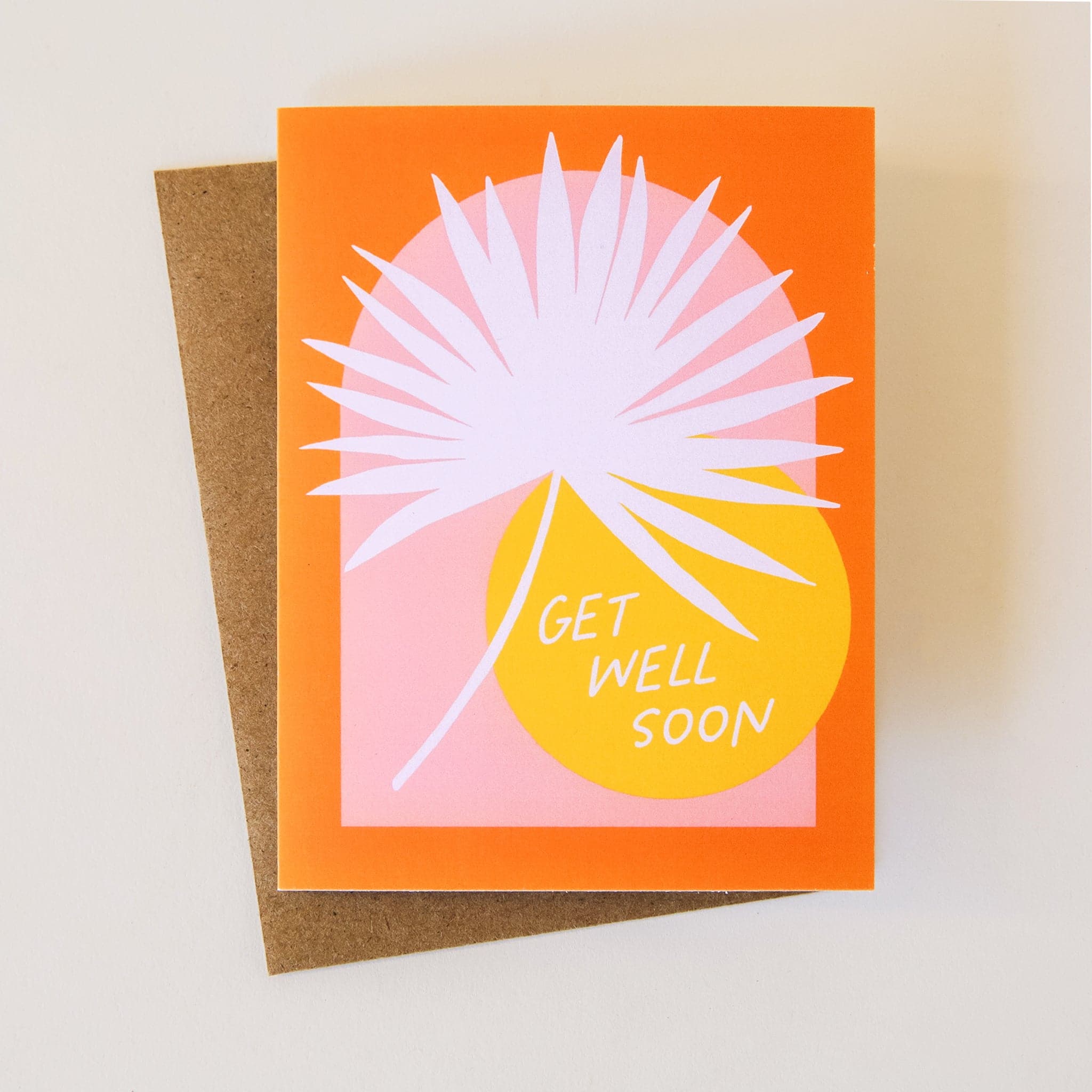A bright orange card wih a light pink arch as well as a white palm and a yellow circle. The card reads, "Get Well Soon".