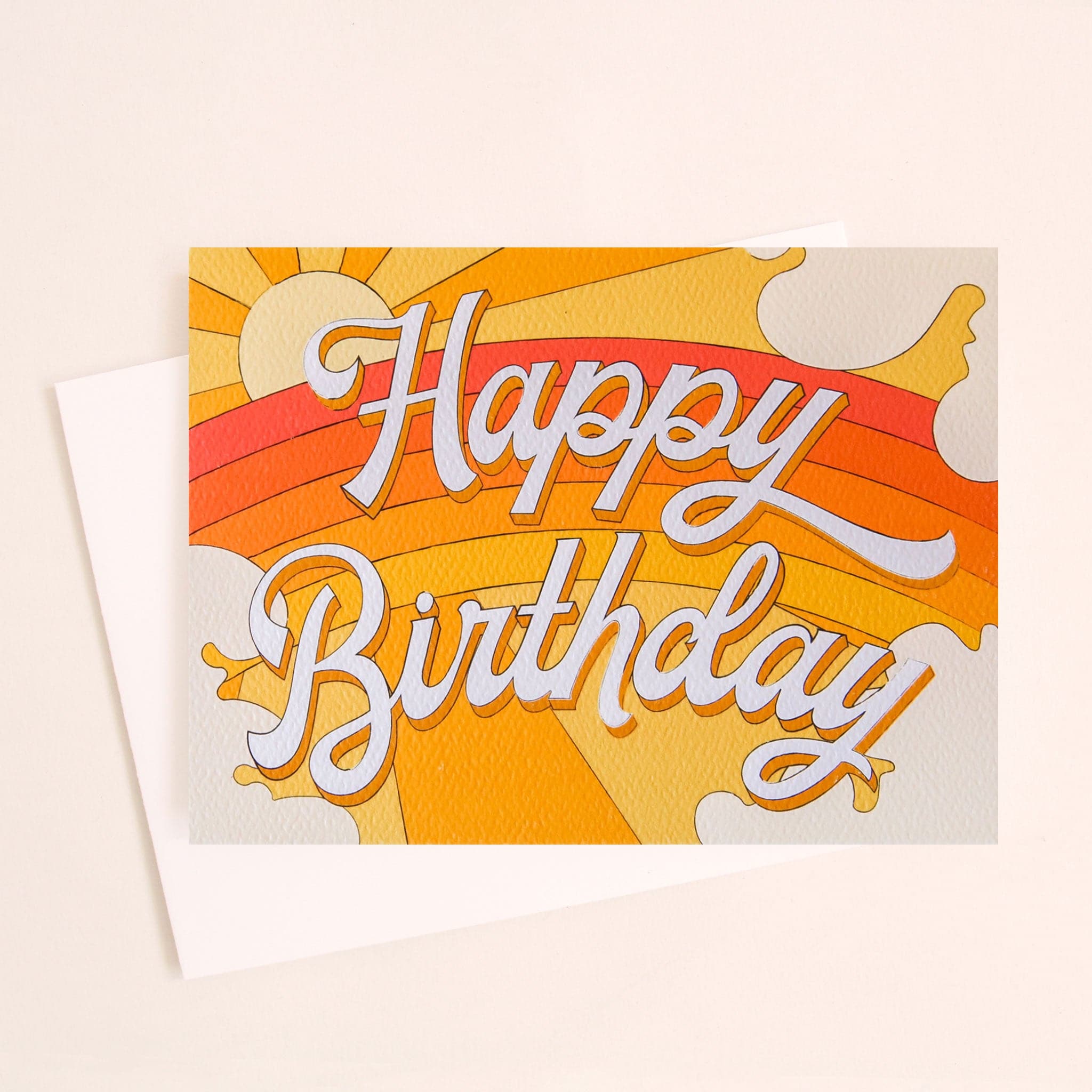 A folded card that has a rainbow graphic made with shades of yellow, orange and red along with text that reads, "Happy Birthday" in white letters across the front.