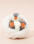 On a cream background is a penguin stuffed animal with a white boucle bed.