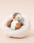 On a cream background is a penguin stuffed animal with a white boucle bed.