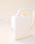 An ivory plastic watering can with a narrow spout and square handle and a rectangle breeze block design on the sides.