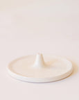 A white incense holder that has a circular shape with a point in the center that is raised with a hole to place your incense in.