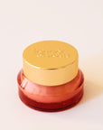 Lip scrub in an orange red container with a gold lid. This lip scrub is grainy, hydrating and perfect for your lips.