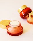 Lip scrub in an orange red container with a gold lid. This lip scrub is grainy, hydrating and perfect for your lips.