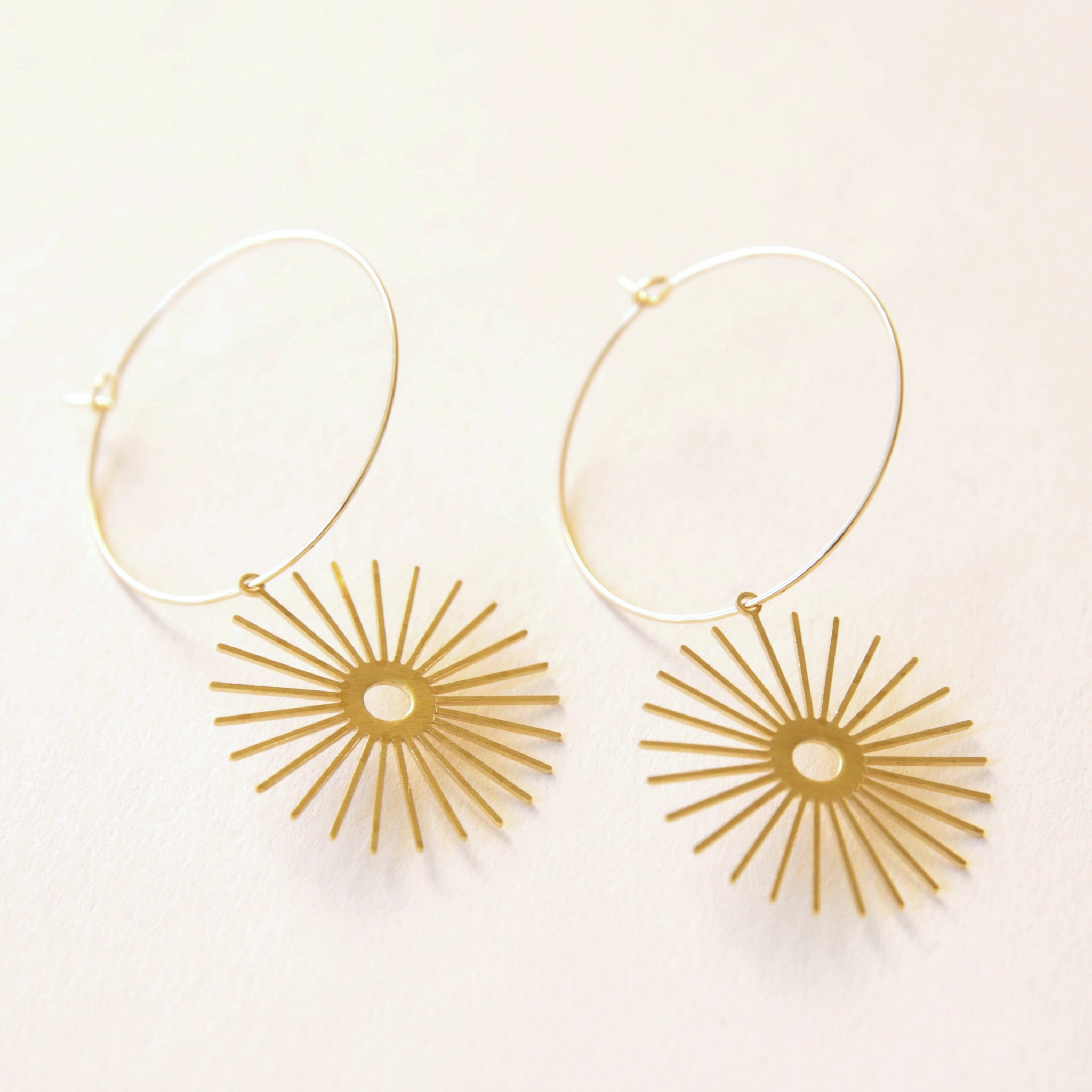 Thin gold hoops with a thin gold sun charm dangling from the bottom.