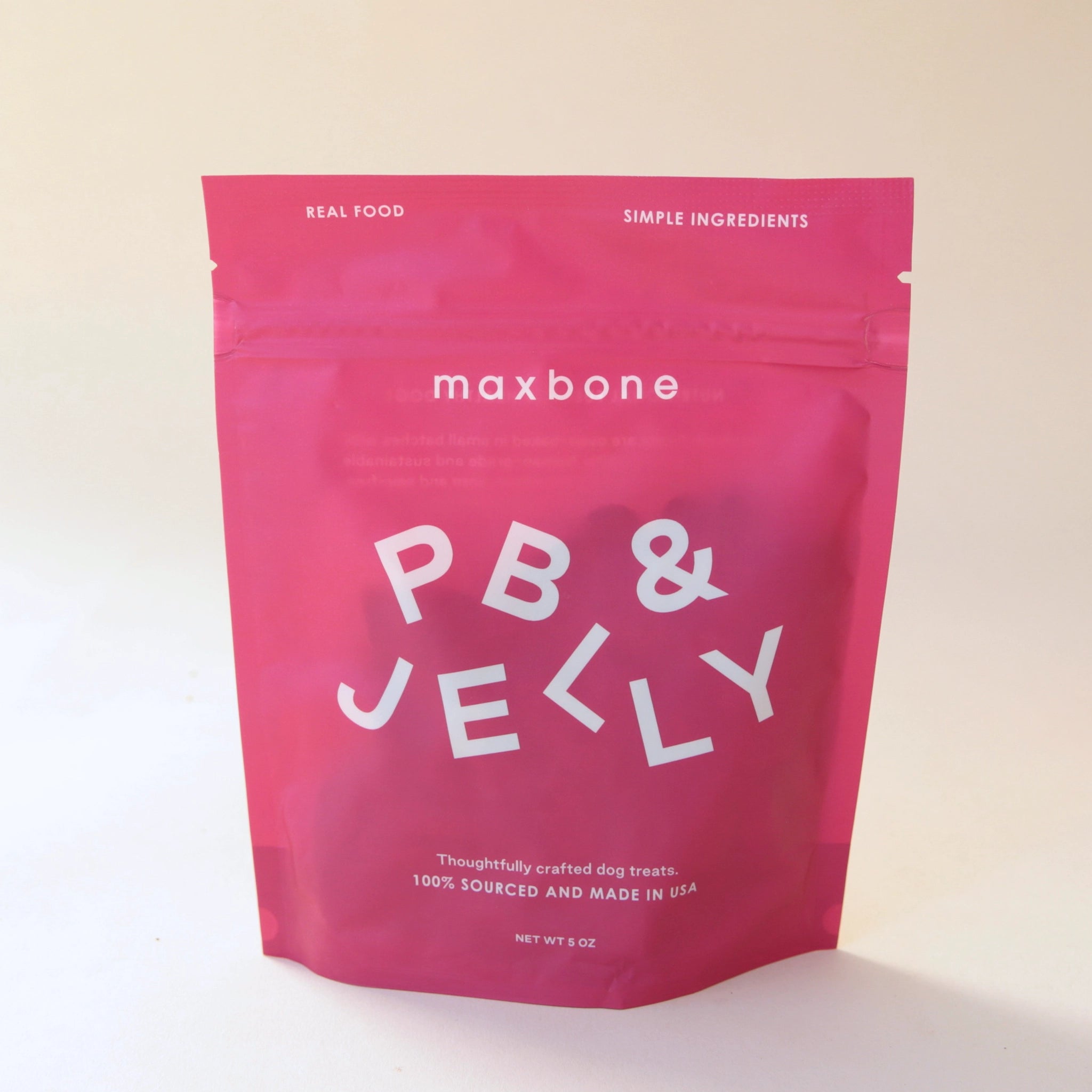 A hot pink packaging with peanut butter and jelly flavored dog biscuits inside. The writing on the front reads, &quot;Maxbone PB &amp; Jelly Thoughtfully crafted dog treats 100% Sourced and Made in the USA&quot; in white text.