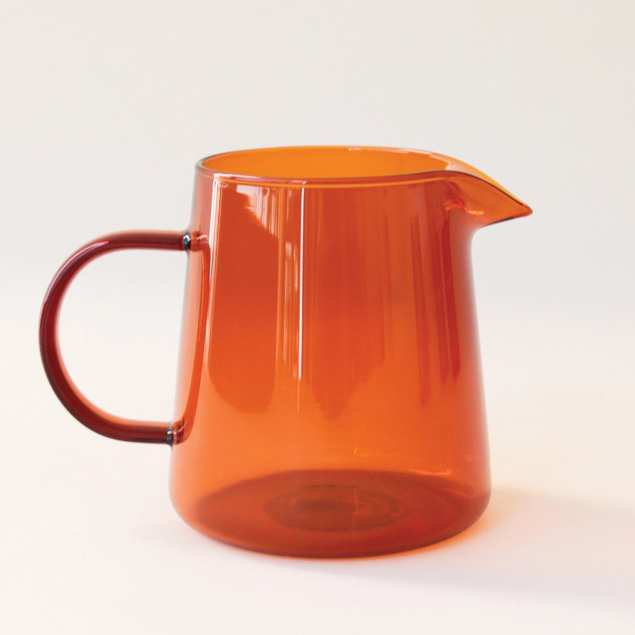 On a white background is a glass amber pitcher. 