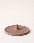 A brown incense holder that has a circular shape with a point in the center that is raised with a hole to place your incense in.