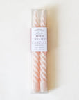 Pair of two blush pink, twisted taper candles with white cotton wicks lay beside each other fasted in clear plastic packaging. The packaging reads 'Blush Tapered Twisted Candles'